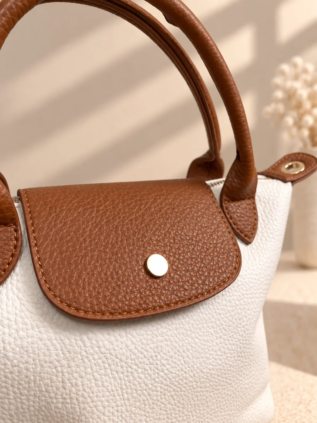 Pormenor da aba castanha com botão dourado da bolsa Lia